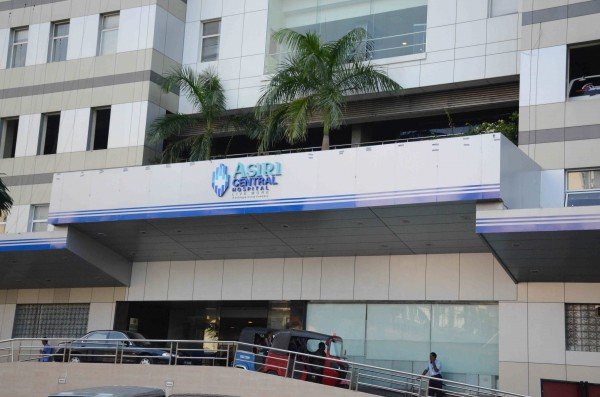 Exterior of the ASRI Central Medical Center building with a sign and palm trees on the roof.