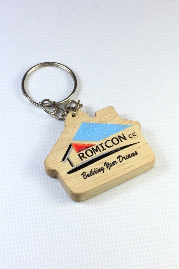 Wooden keychain with a logo for ROMICON CC and the slogan 'Building Your Dreams' on a white background.