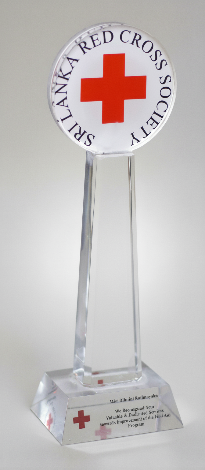 A glass award trophy with the Red Cross emblem and the words 'SPIRIT OF A RED CROSS SOCIETY' encircling it, and an inscription on the base recognizing a contribution.