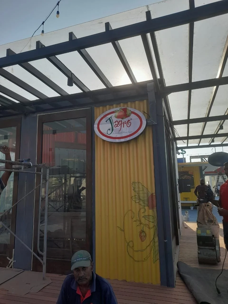 Exterior of a building with a sign saying 'Jaro' with strawberries, and a yellow wall with a illustration of strawberry plants.