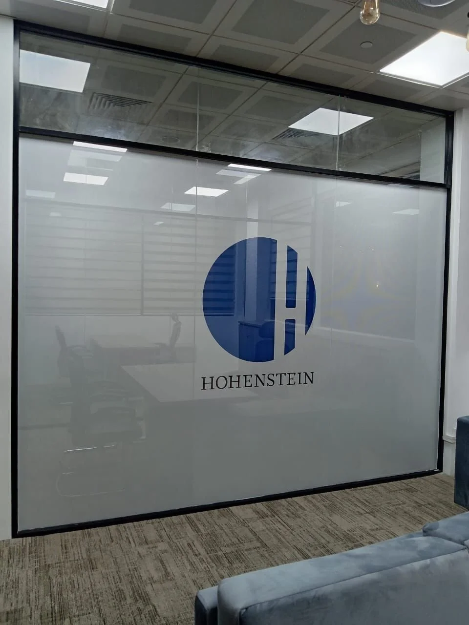Office conference room with frosted glass wall featuring a blue circle logo and the name 'Hohenstein'.