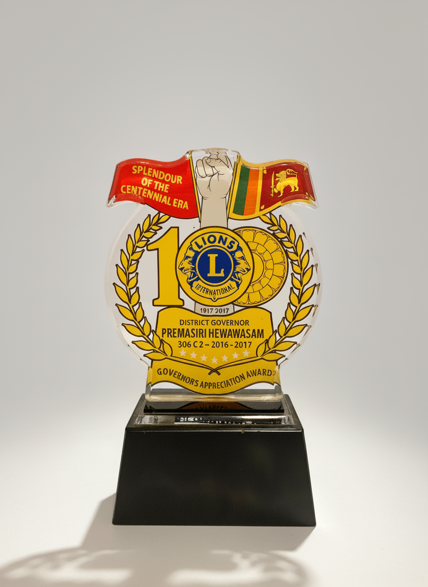 A commemorative glass trophy with colorful flags and text, honoring District Governor Premasiri Hewawasa for his term from 2016 to 2017, celebrating 100 years of Lions International.