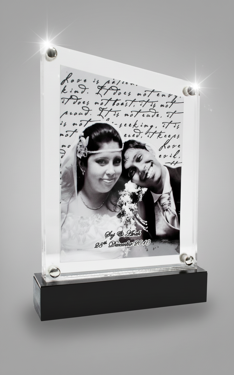 Black and white wedding photo of a bride and groom, with handwritten text above and below, displayed in a glass frame on a black base.
