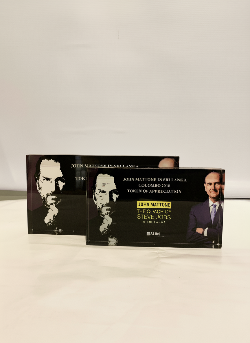Two boxes labeled 'John Mattone in Sri Lanka, Column 2018, Token of Appreciation' with a picture of Steve Jobs on the right side of each box, placed on a white surface against a plain white background.