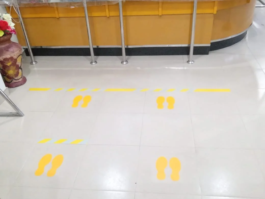 Floor markers indicating social distancing at a counter in a public space, with yellow footprints and dashed lines.