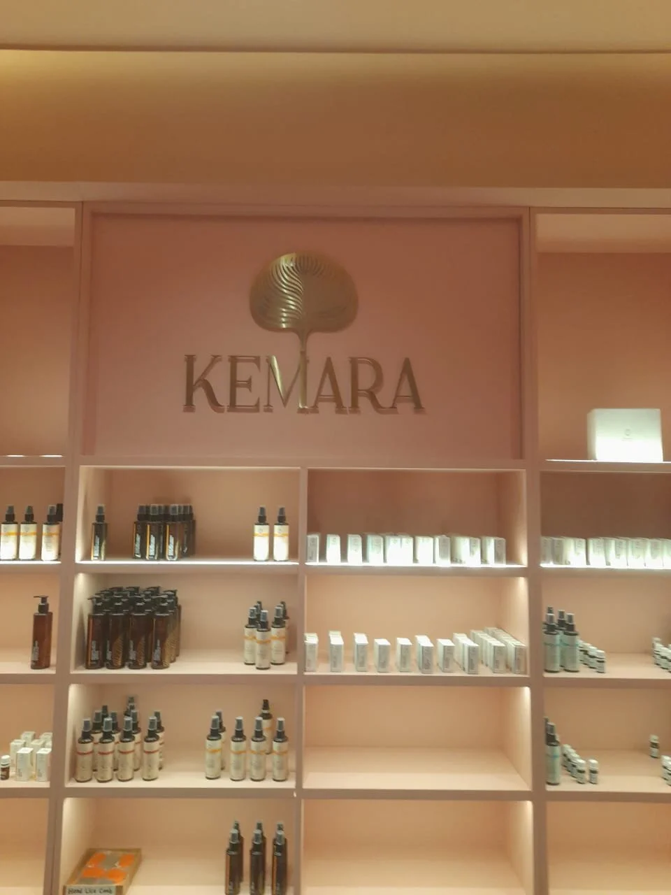 Retail display shelves with skincare products in bottles and boxes, with a prominent 'KEMARA' sign and a logo above.