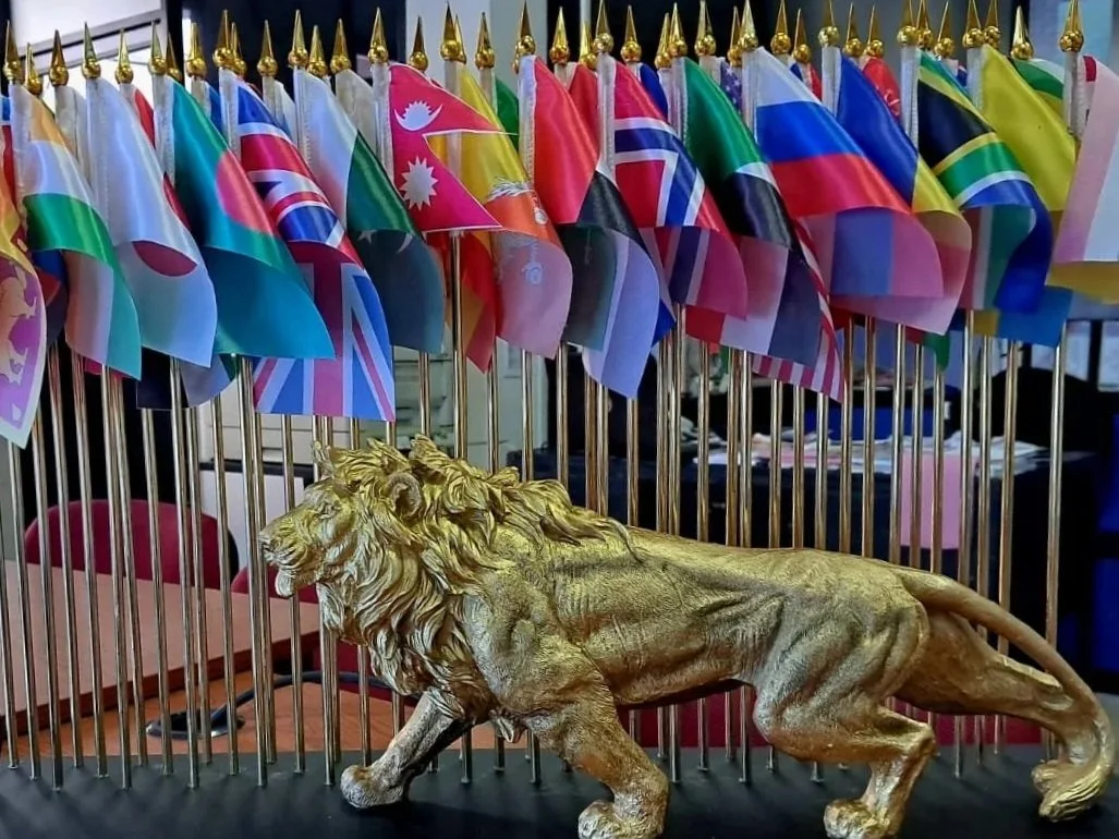 Golden lion statue in front of a row of small international flags with colorful patterns.