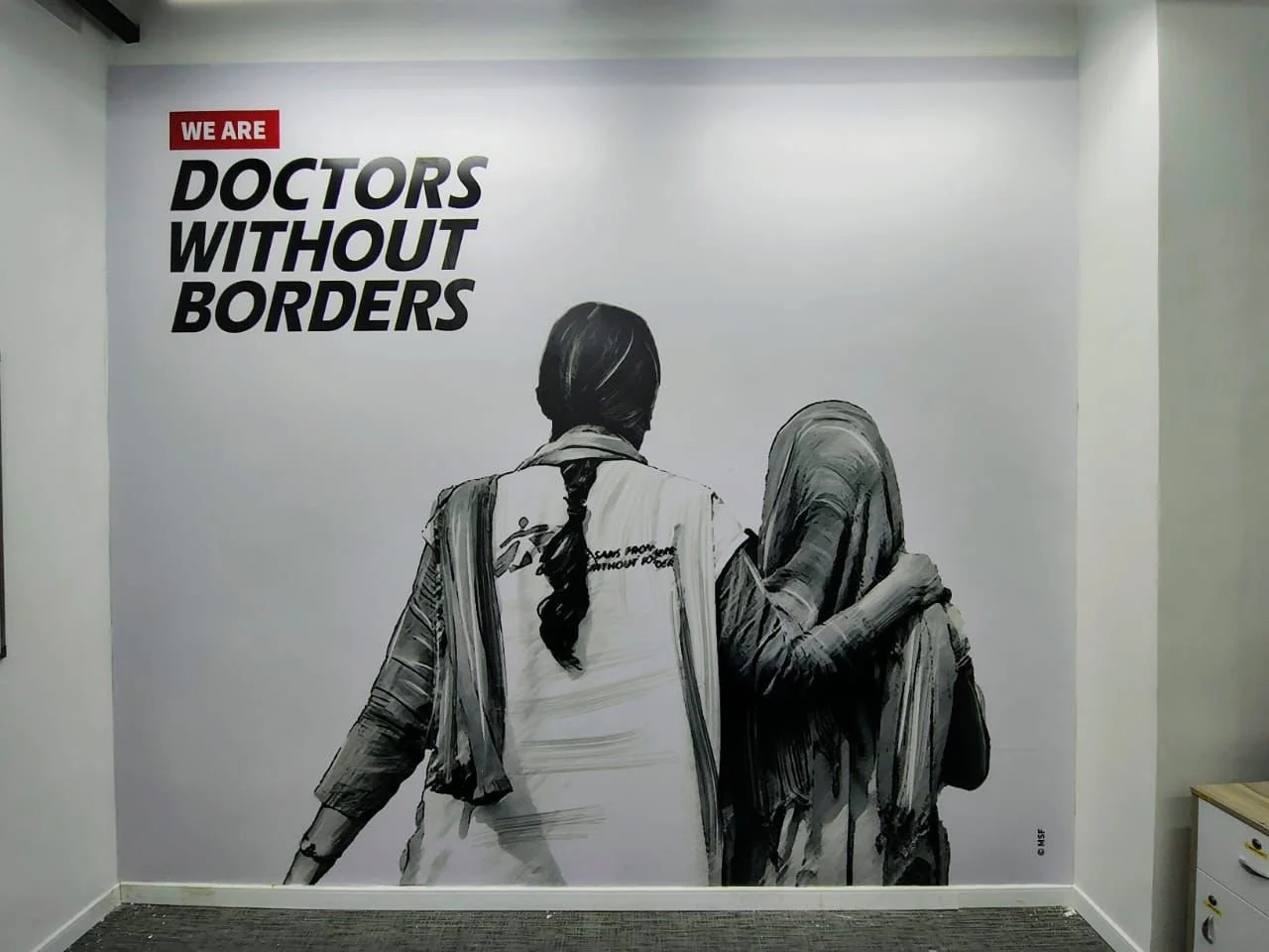Wall mural of two women walking together, one in a headscarf, with text "WE ARE DOCTORS WITHOUT BORDERS" in bold black and red font.