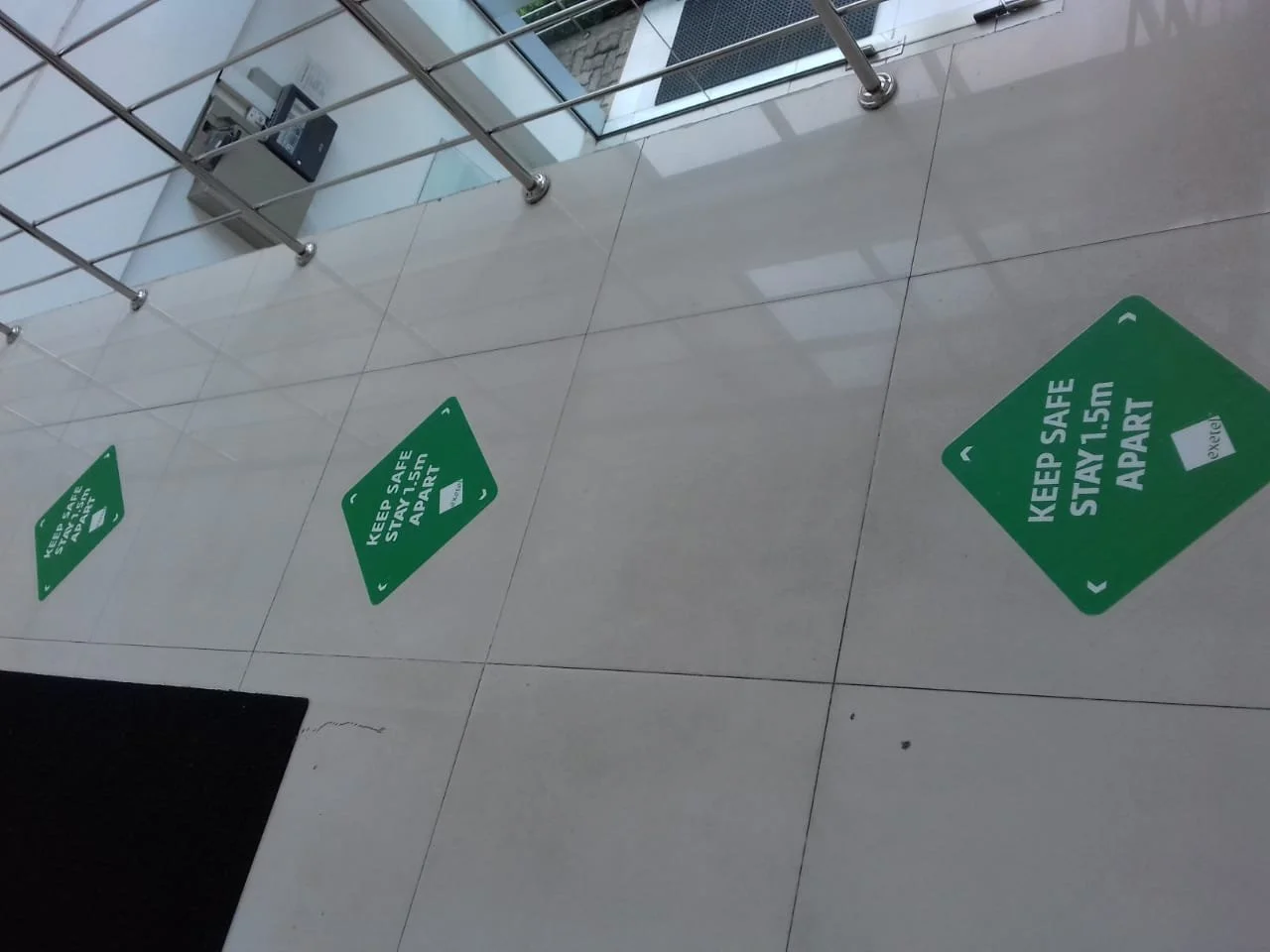 Green floor stickers on a tiled floor that read 'Keep Safe Stay 1.5m Apart' and have arrows pointing in different directions.