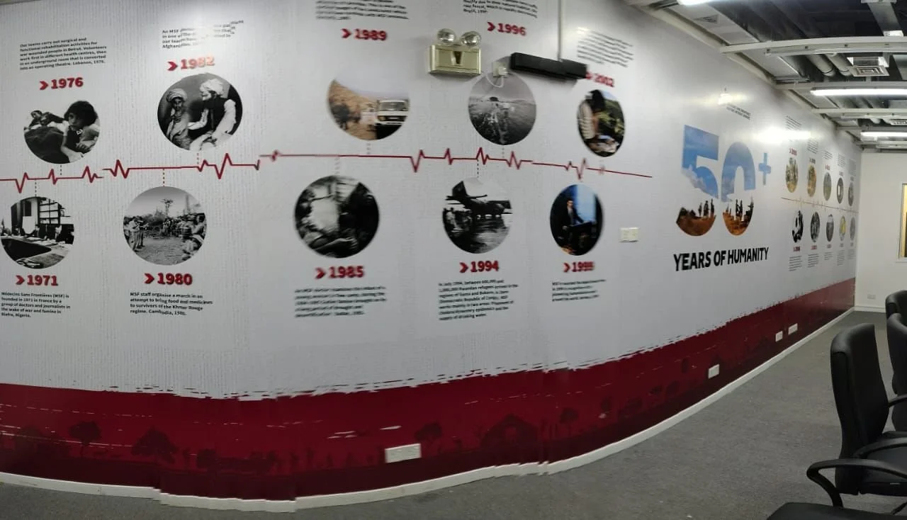 Wall mural displaying a timeline of historical events related to humanity, with dates and images, from 1971 to 1996, and a large '50+ years of humanity' graphic.