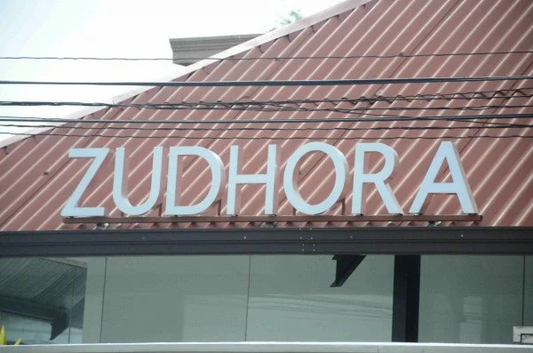 Sign reading 'ZUDHORA' on the exterior of a building with a brown, ridged metal roof.