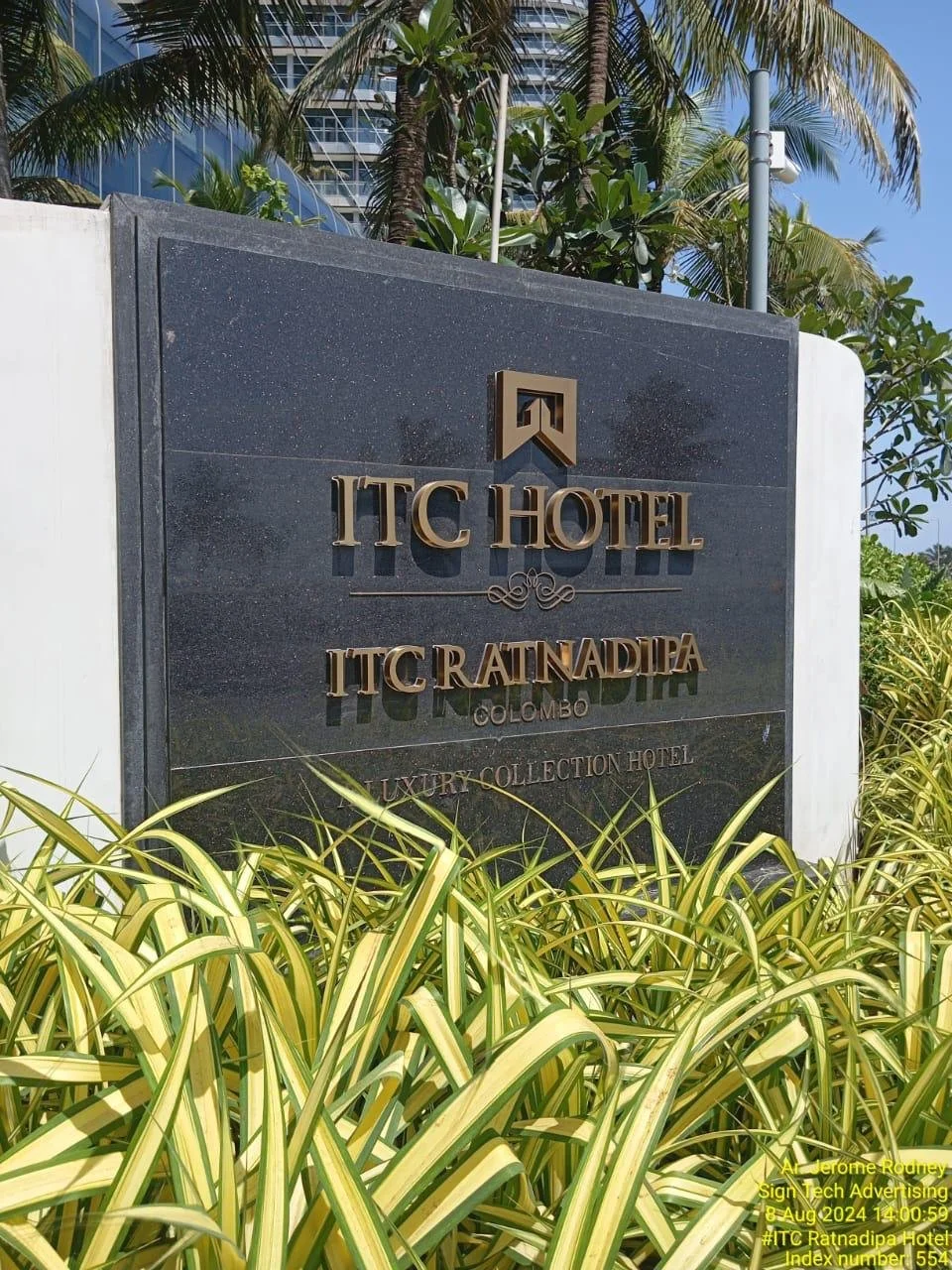 Sign for ITC Hotel located in Colombo, Sri Lanka, surrounded by green plants and palm trees, with a modern building in the background.