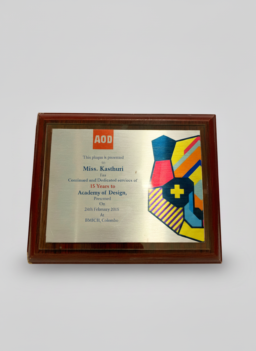 A framed plaque with a colorful abstract design and text honoring Miss. Kashturi for 15 years of service at the Academy of Design in Colombo, presented on February 24, 2015.