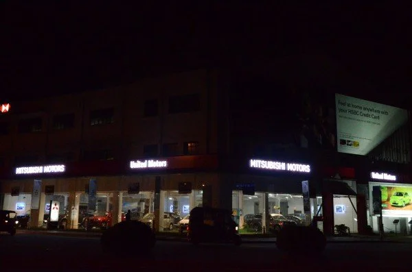 Nighttime exterior view of a Mitsubishi Motors dealership with illuminated signage and cars displayed inside.