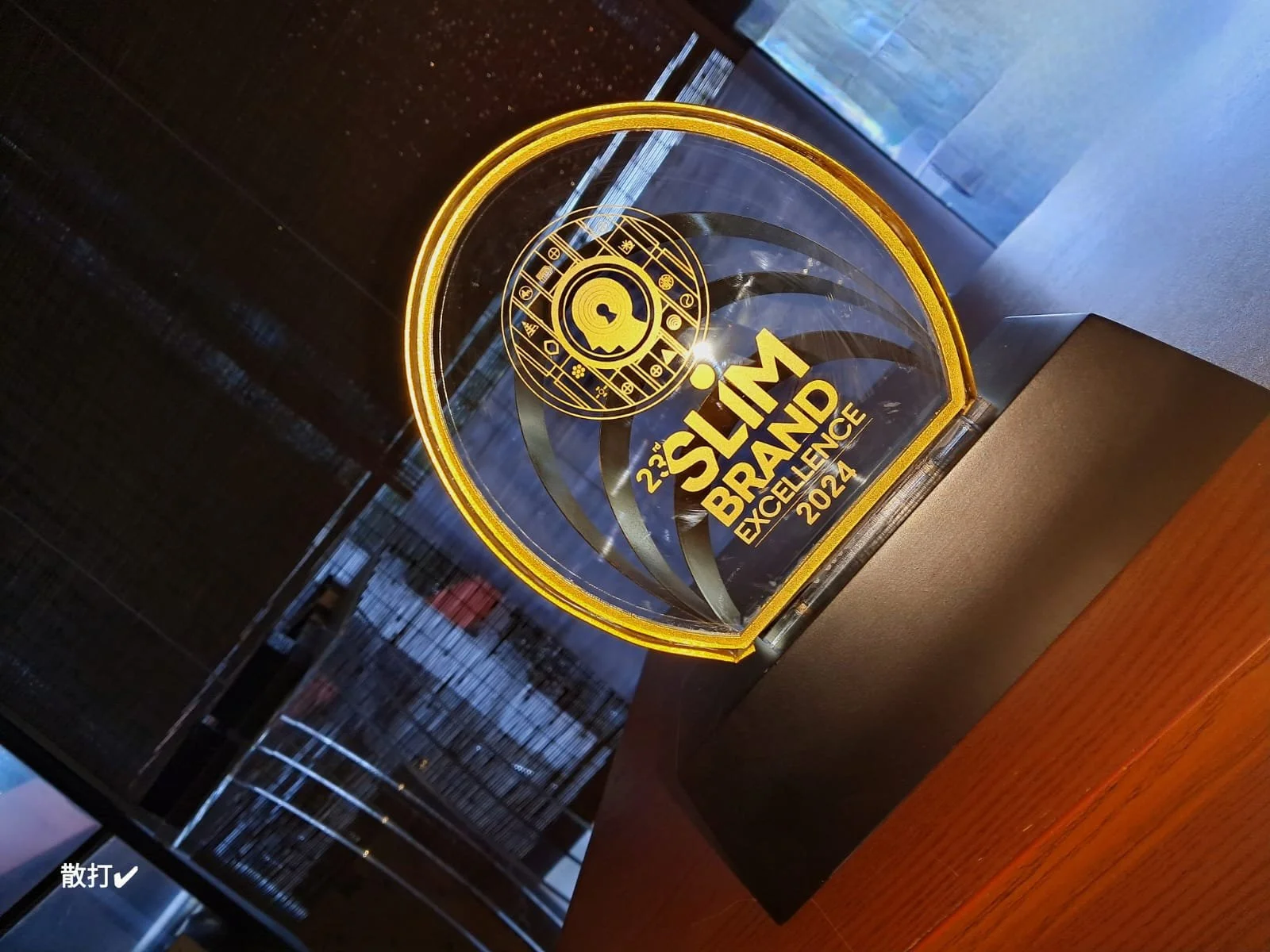A glass award or trophy with the text "23rd SLTM Brain Excellence 2024" in gold, featuring a logo with a brain and symbols, illuminated with yellow light.