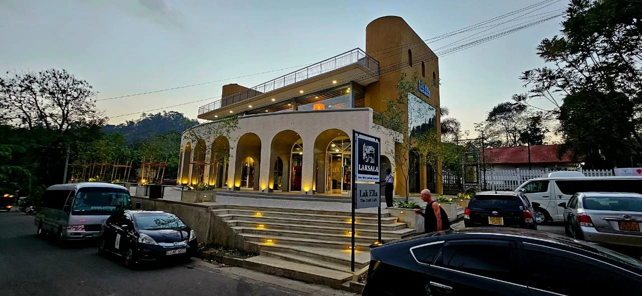 Exterior of a modern building with arches and a tower-like structure, surrounded by parked cars and trees at dusk.
