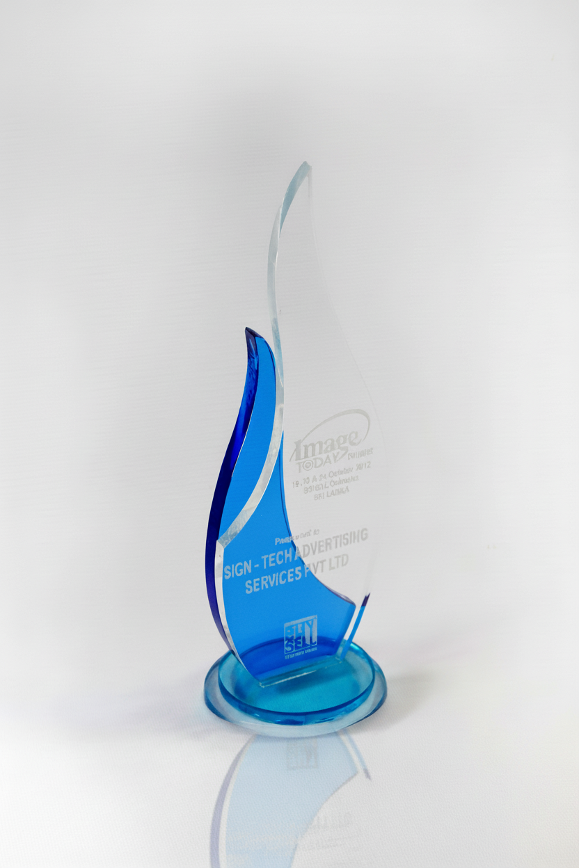 Blue and clear glass award with a wavy design, inscribed with text and logo, standing on a round base.
