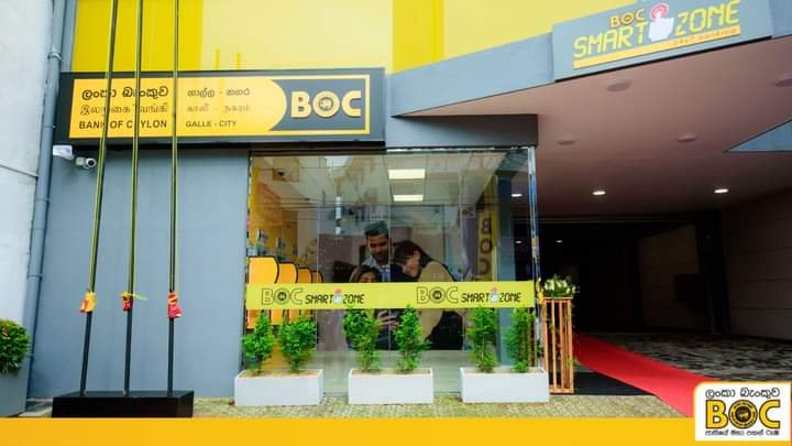 People inside a store called BOC in Galle City, Sri Lanka, with signs for BOC Smart Zone, green plants outside, and a red carpet leading inside.