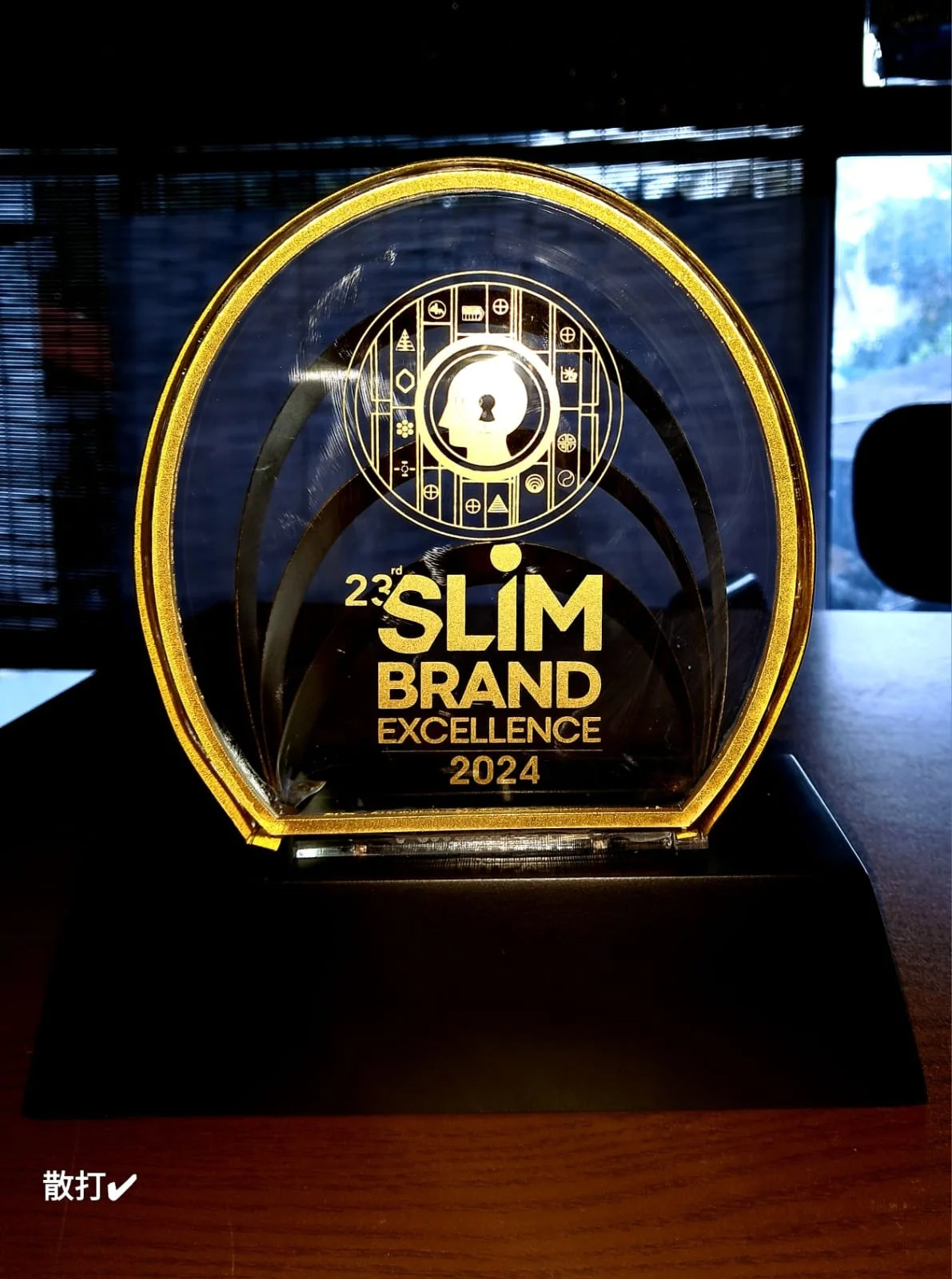 A glass award with gold accents, inscribed with the text '23rd Slim Brand Excellence 2024', and a silhouette of a head with a keyhole inside.