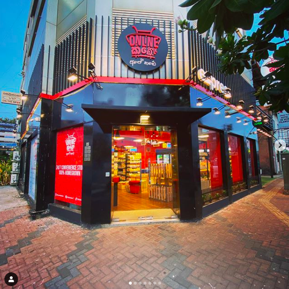 Exterior of a convenience store called 'Online Grocery' with a black and red themed storefront, large glass windows, and interior shelves stocked with products.