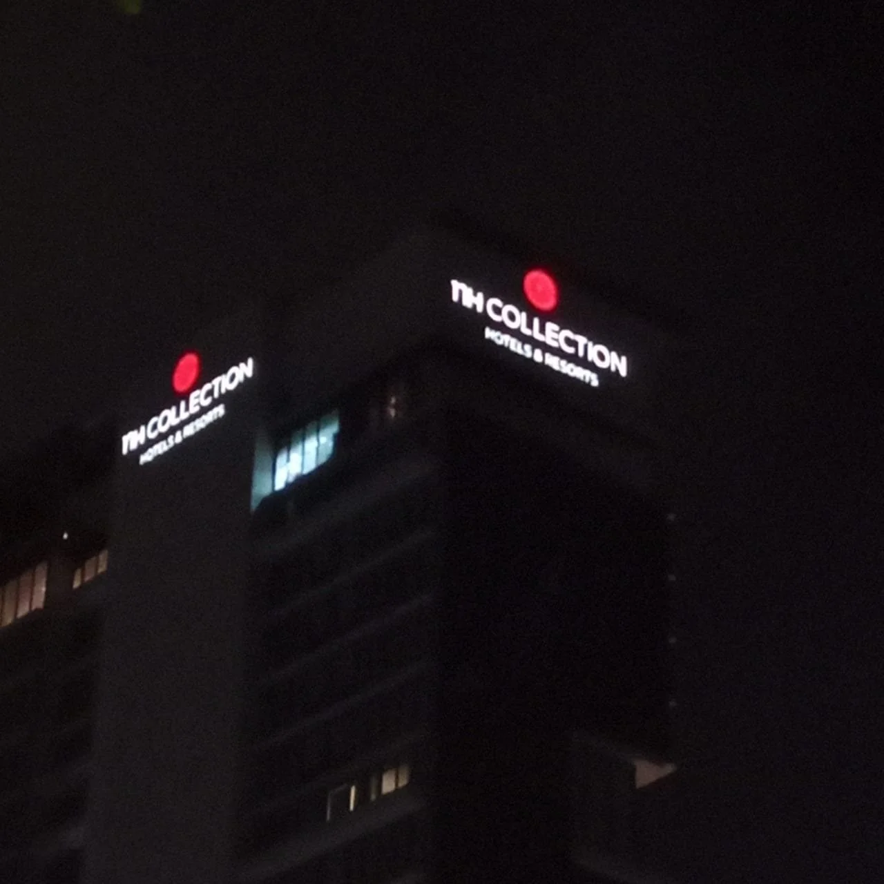 Night view of a tall building with illuminated signs that read 'MY COLLECTION HOTELS & RESORTS' and feature a red logo.
