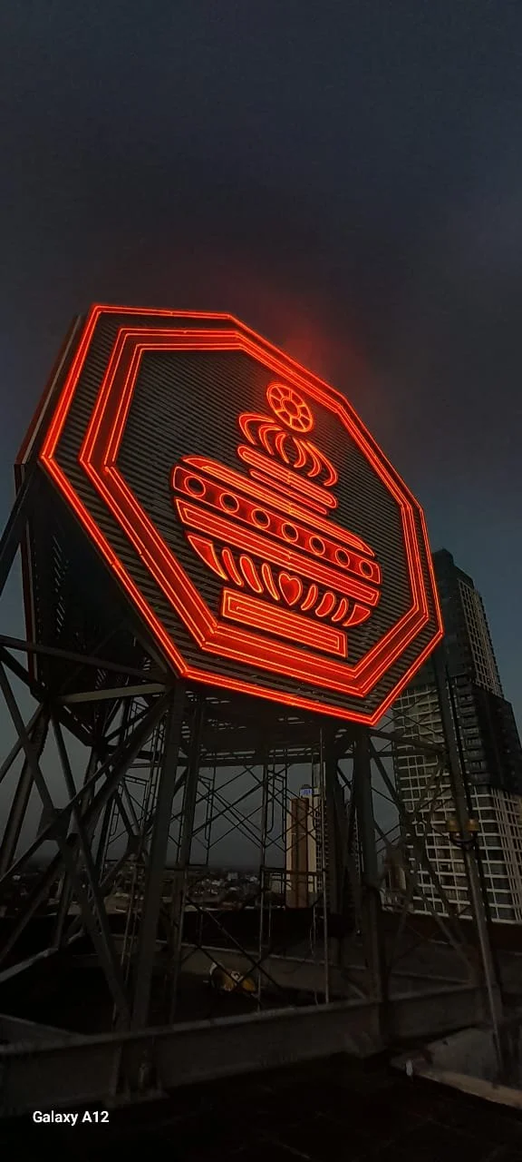 Neon sign of a bowl of ramen with chopsticks on a rooftop at dusk