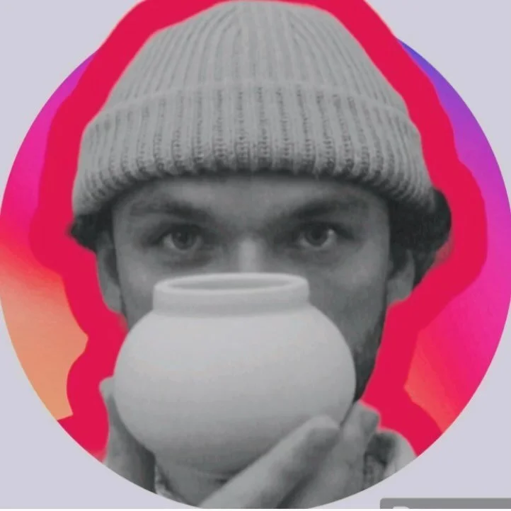 A black and white photo of a young man wearing a knit beanie, looking directly at the camera while holding a small cup close to his mouth.