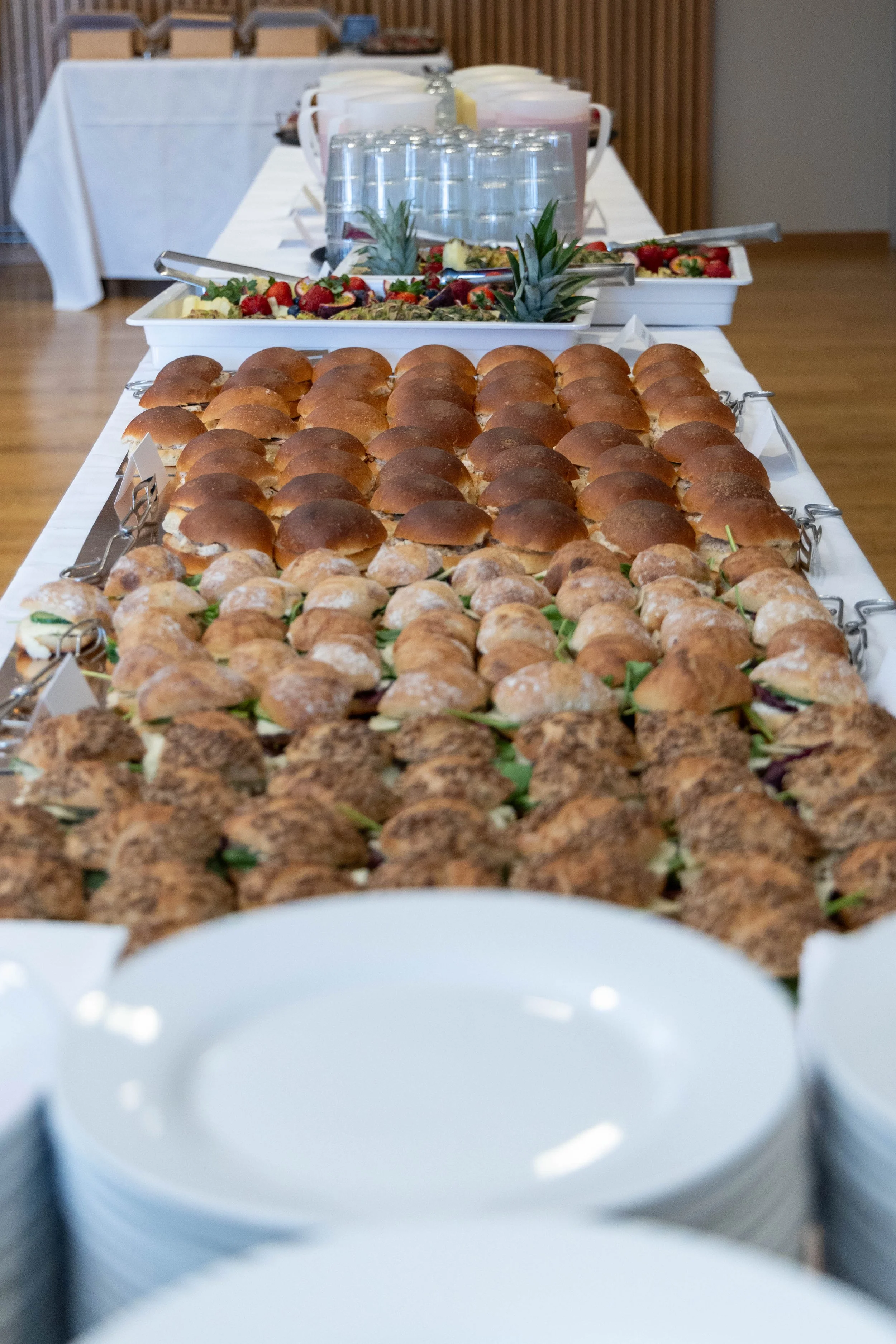 Buffébord med små rounda bröd, croissanter, och kladdkakebollar, samt frukt och brödskålar i bakgrunden.