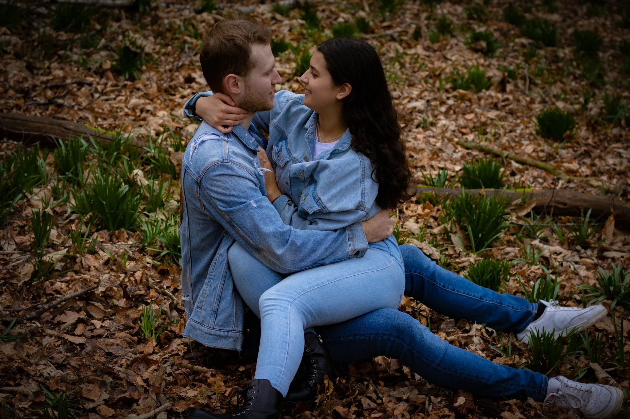 A young couple sitting on the forest floor, embracing each other and smiling.