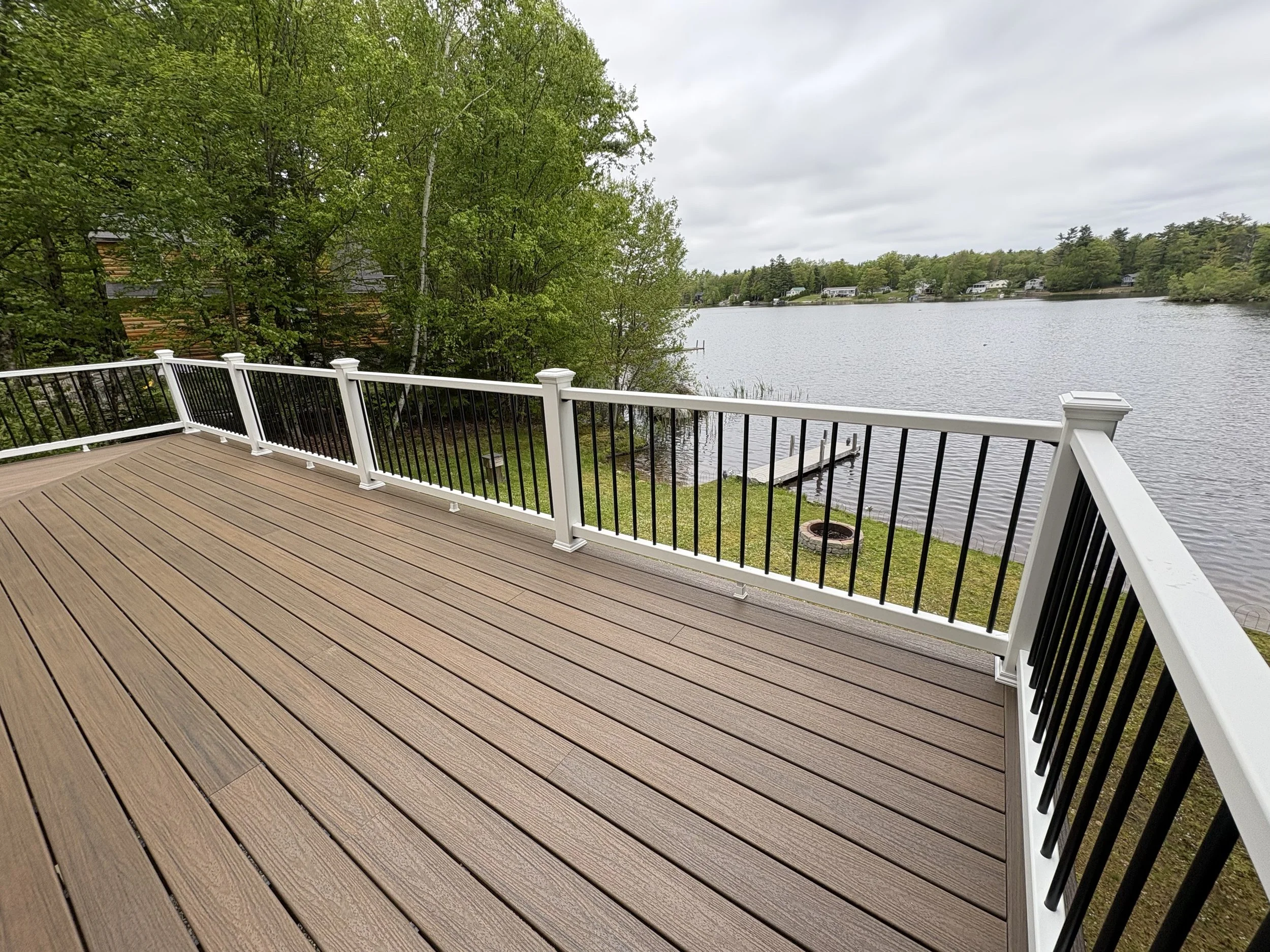 A wooden deck overlooking a body of water with trees and houses in the background.