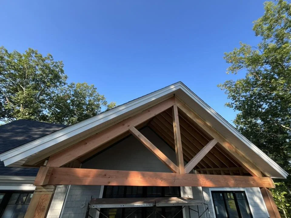 Close-up of a house roof under construction with exposed wooden beams and blue sky in the background.