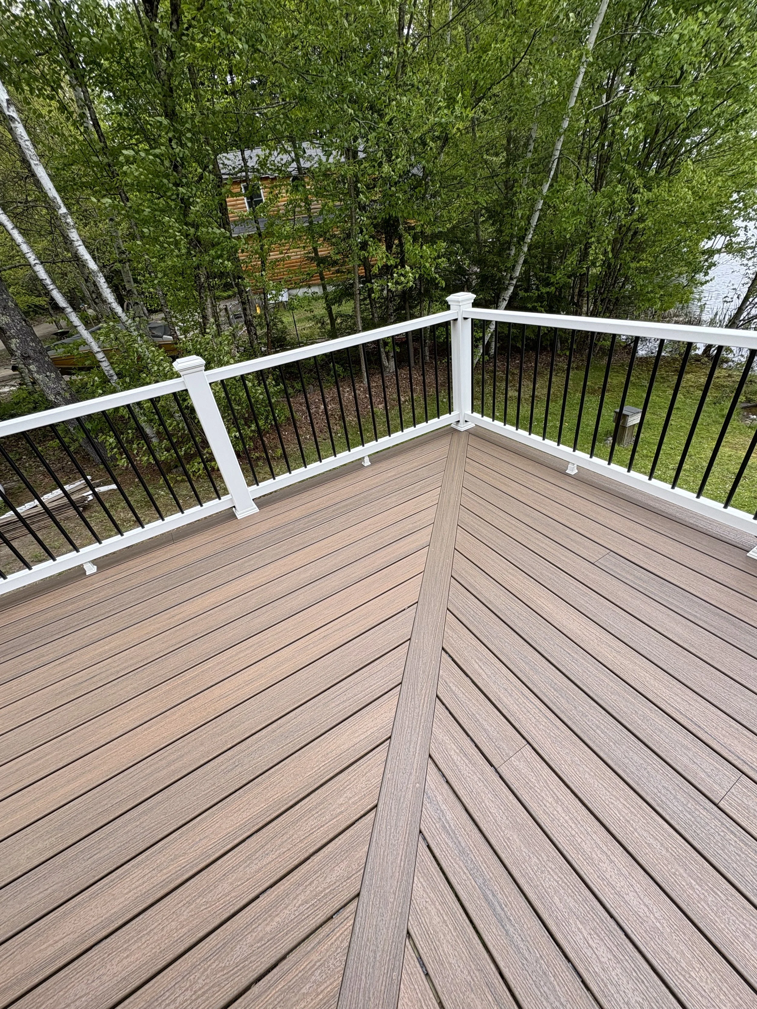 View from a wooden deck with white and black railing, overlooking a green backyard with trees and a neighboring house.