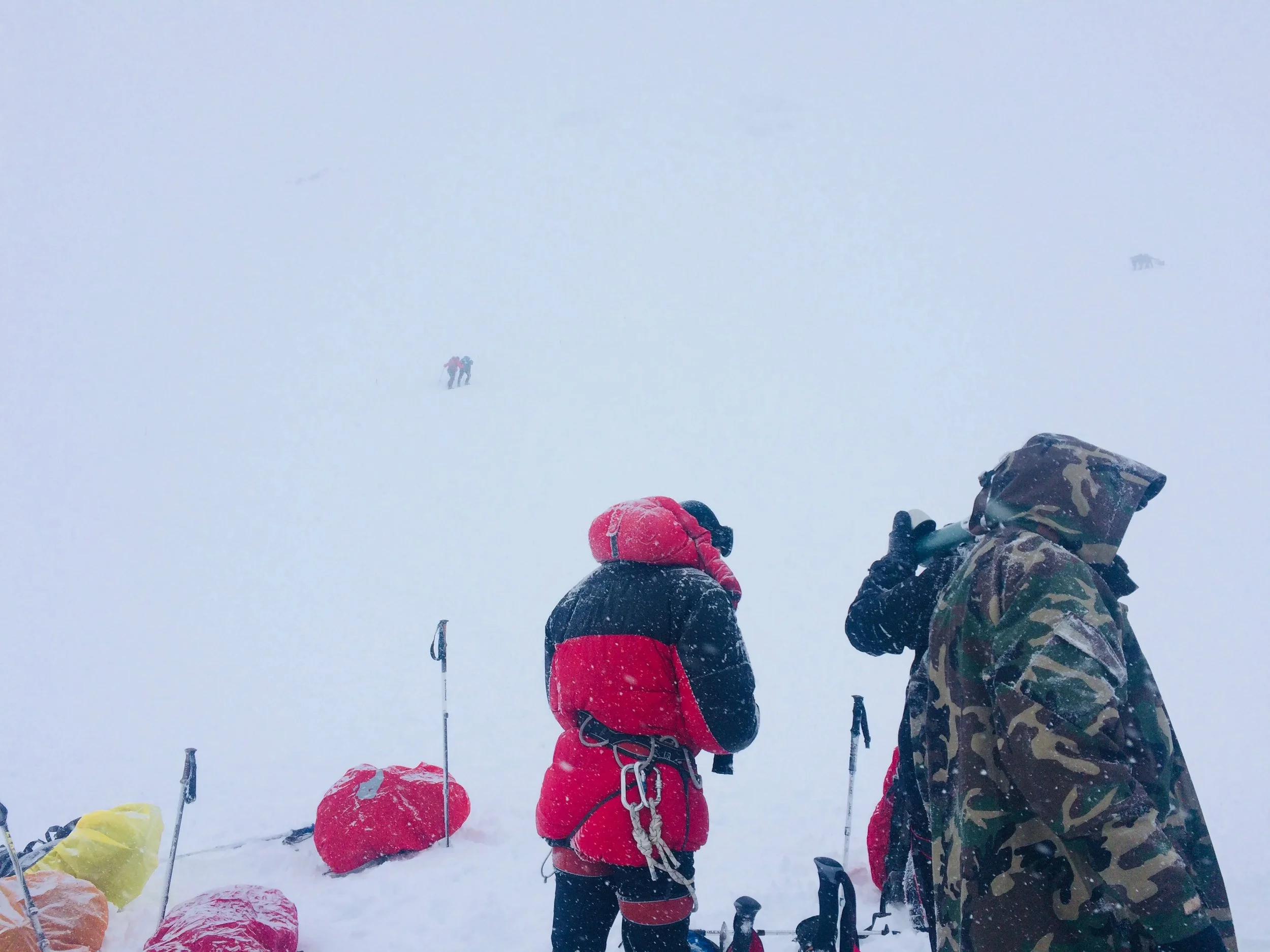 Climbers visible through the snowfall, moving towards fixed rope point
