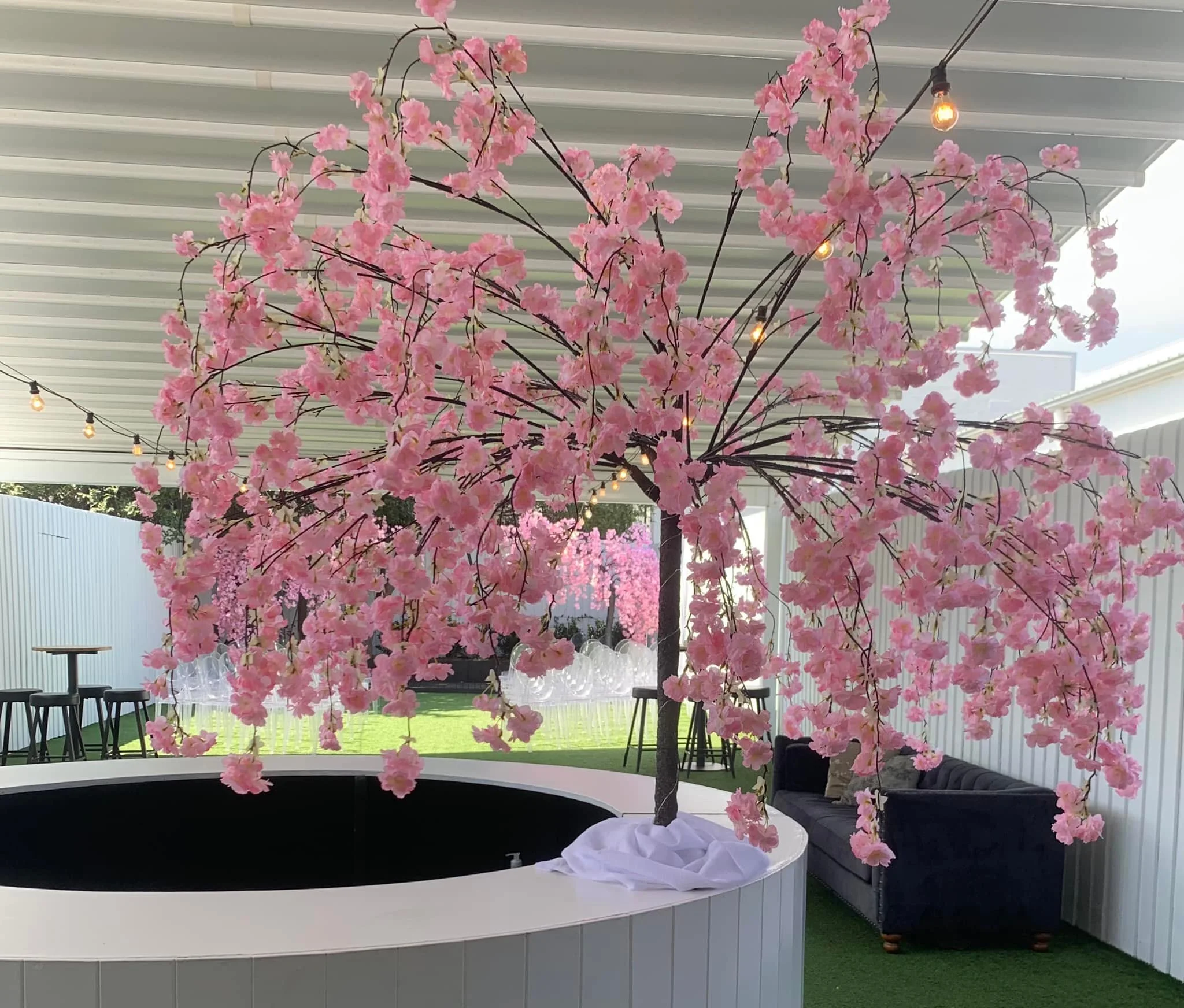 Indoor venue with pink artificial cherry blossom tree, string lights, modern seating area.