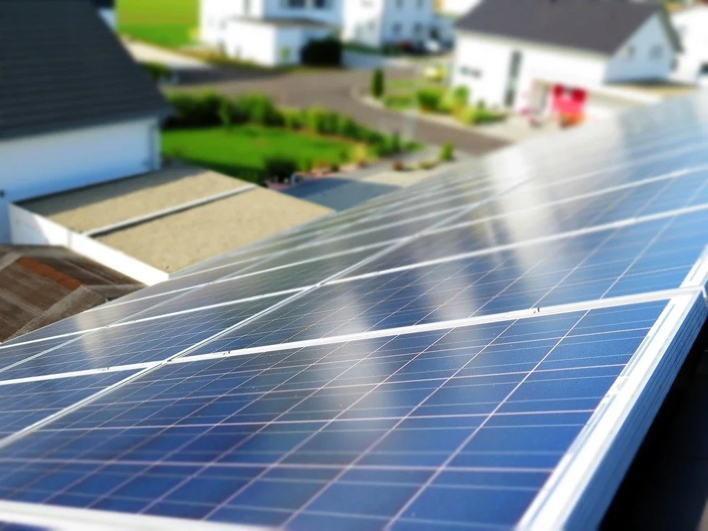 Close-up of solar panels installed on a house roof with a neighborhood of houses and a green lawn in the background.