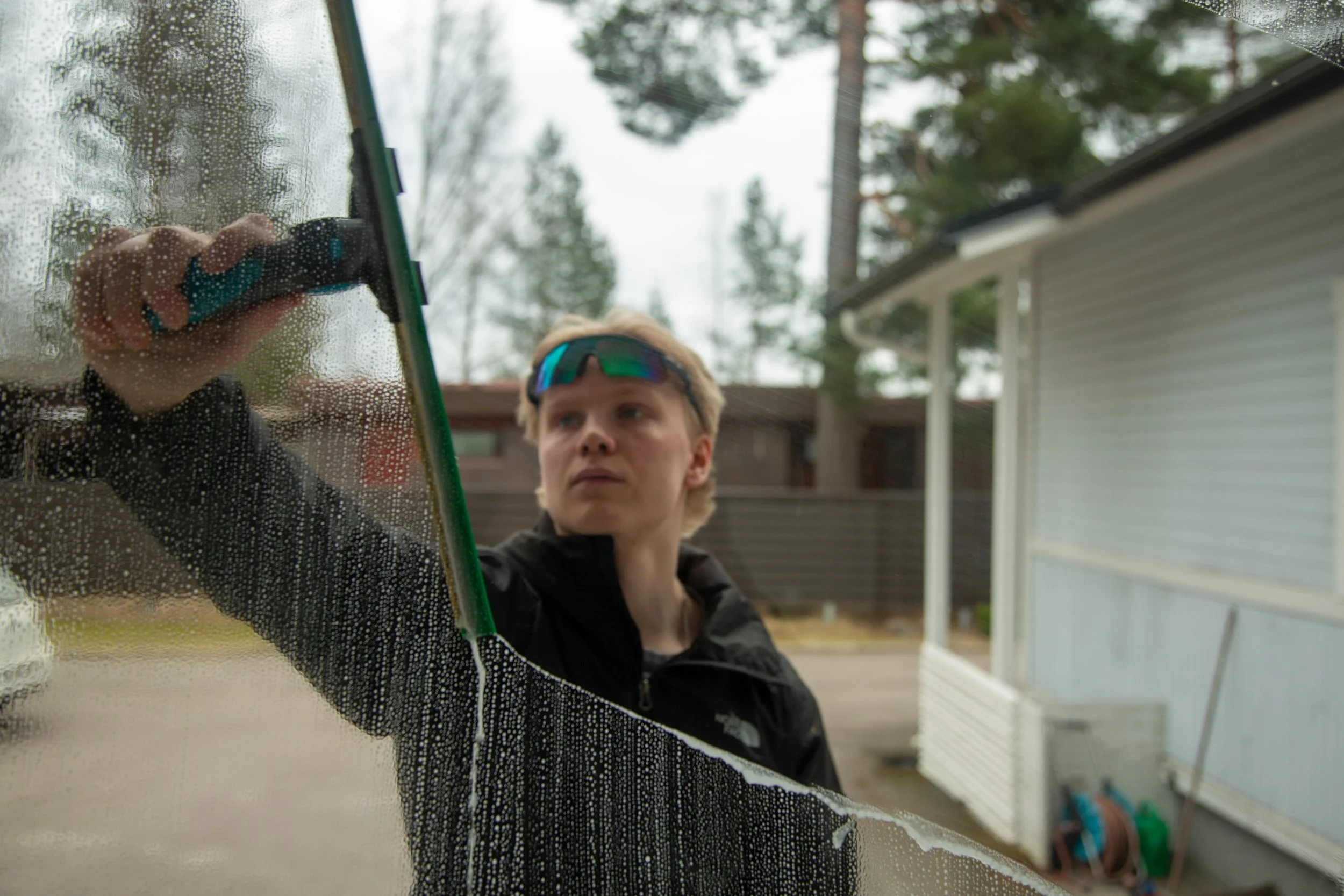 A person cleaning a window with a squeegee outside of a house on a cloudy day.