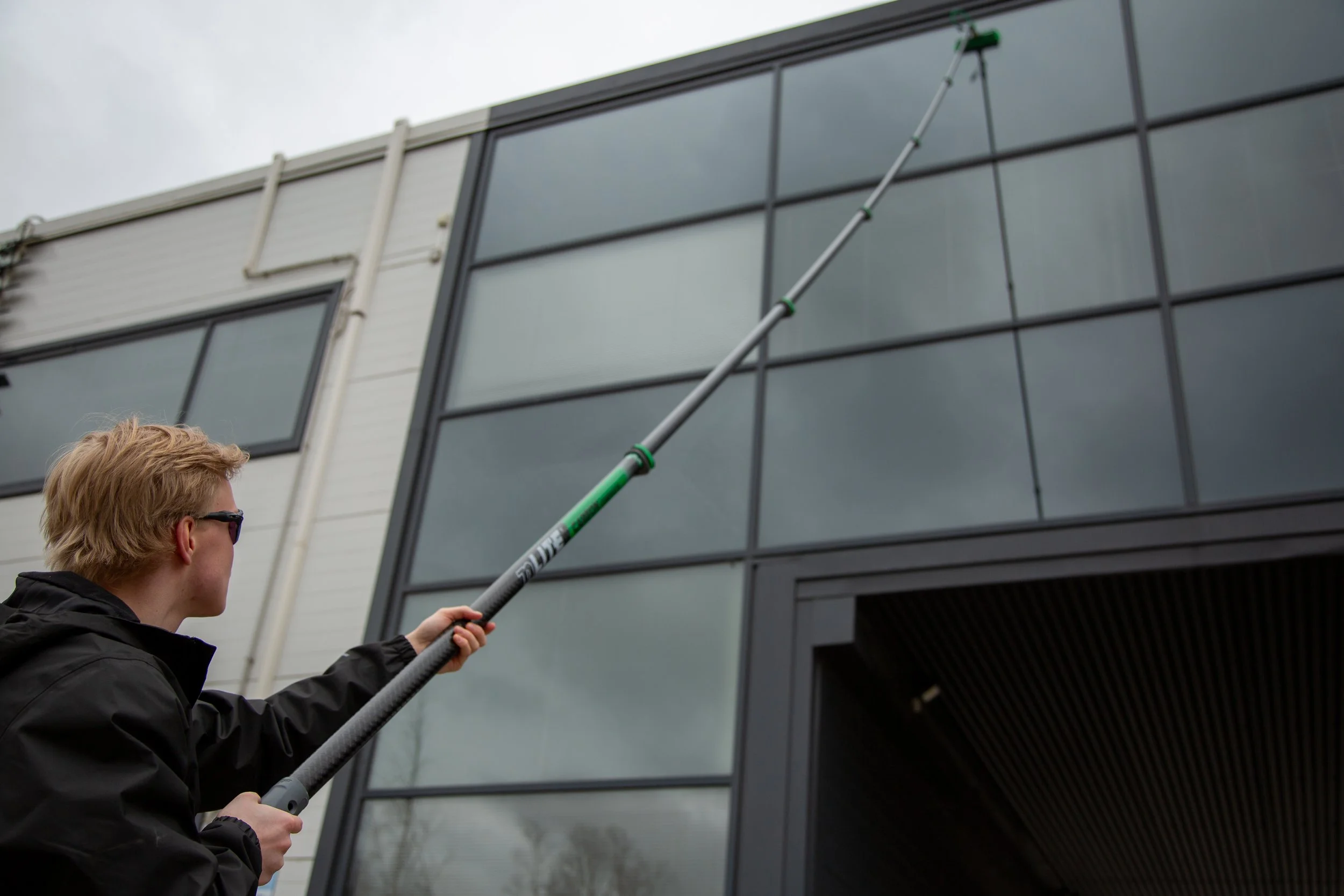 Person cleaning or washing exterior windows of a modern building with a long pole and squeegee.