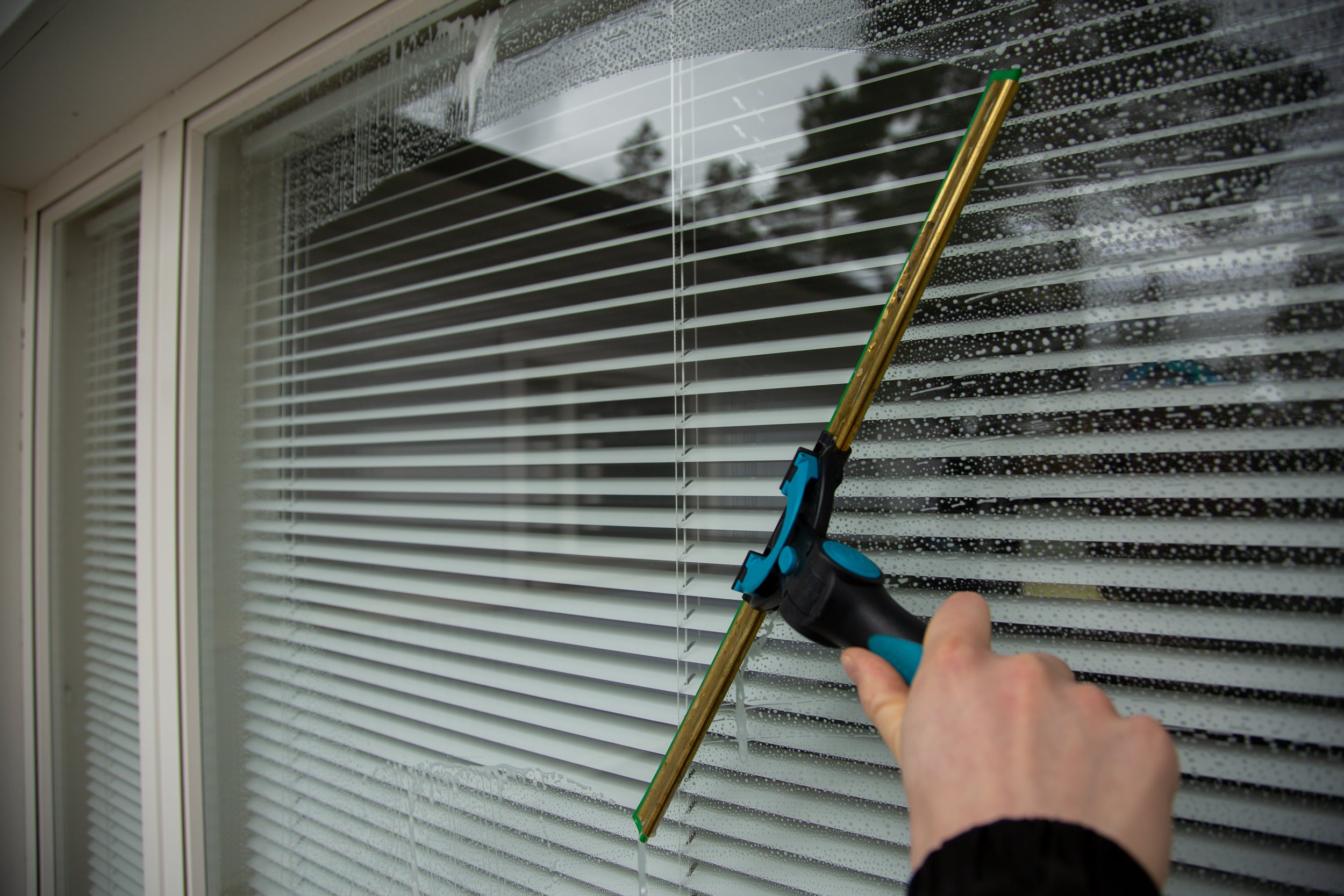 Person cleaning rain droplets off window blinds with a squeegee.