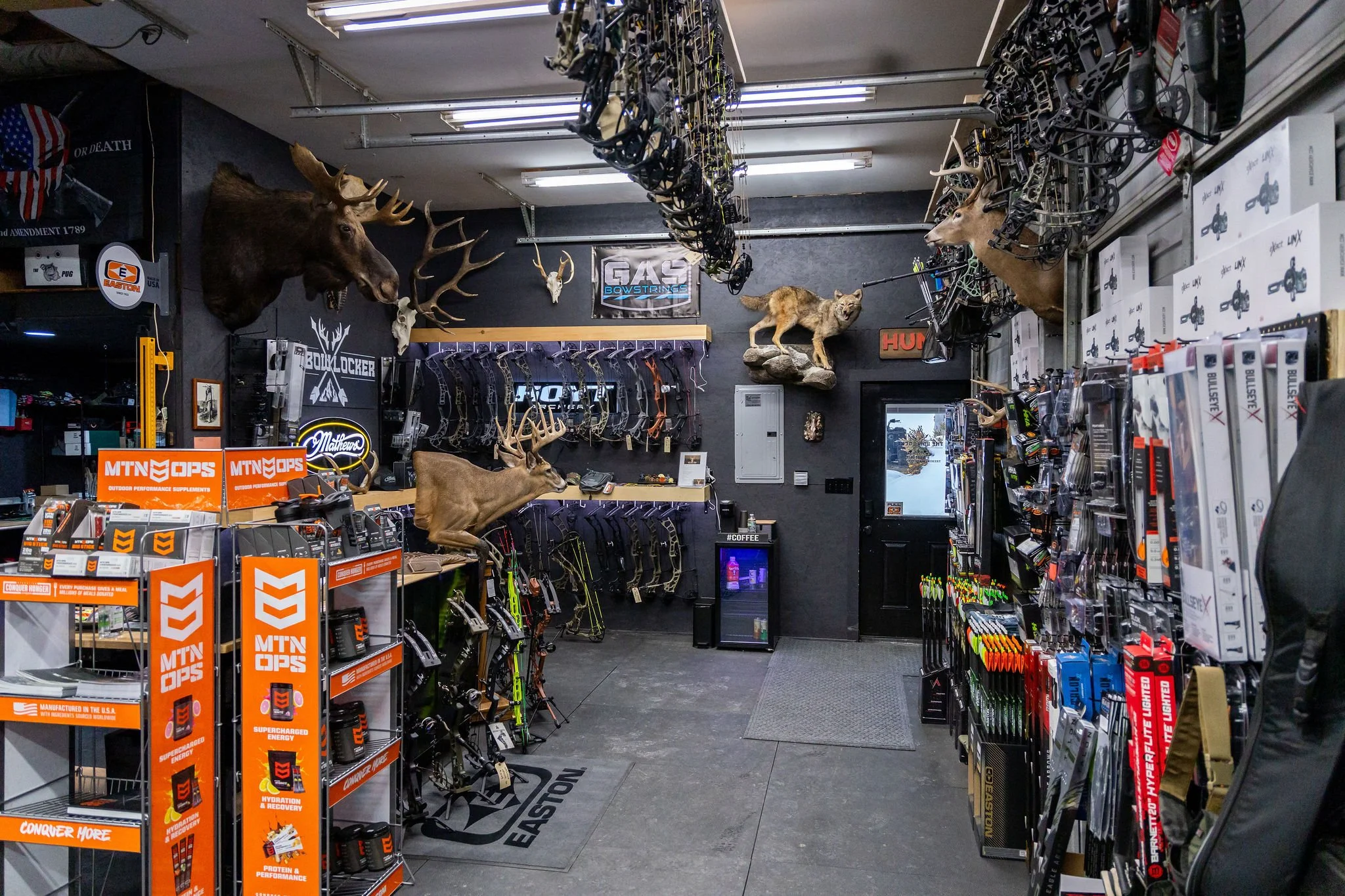 Inside an outdoor sporting goods store with hunting and fishing gear, including mounted animal heads and taxidermy, archery supplies, and various hunting accessories.