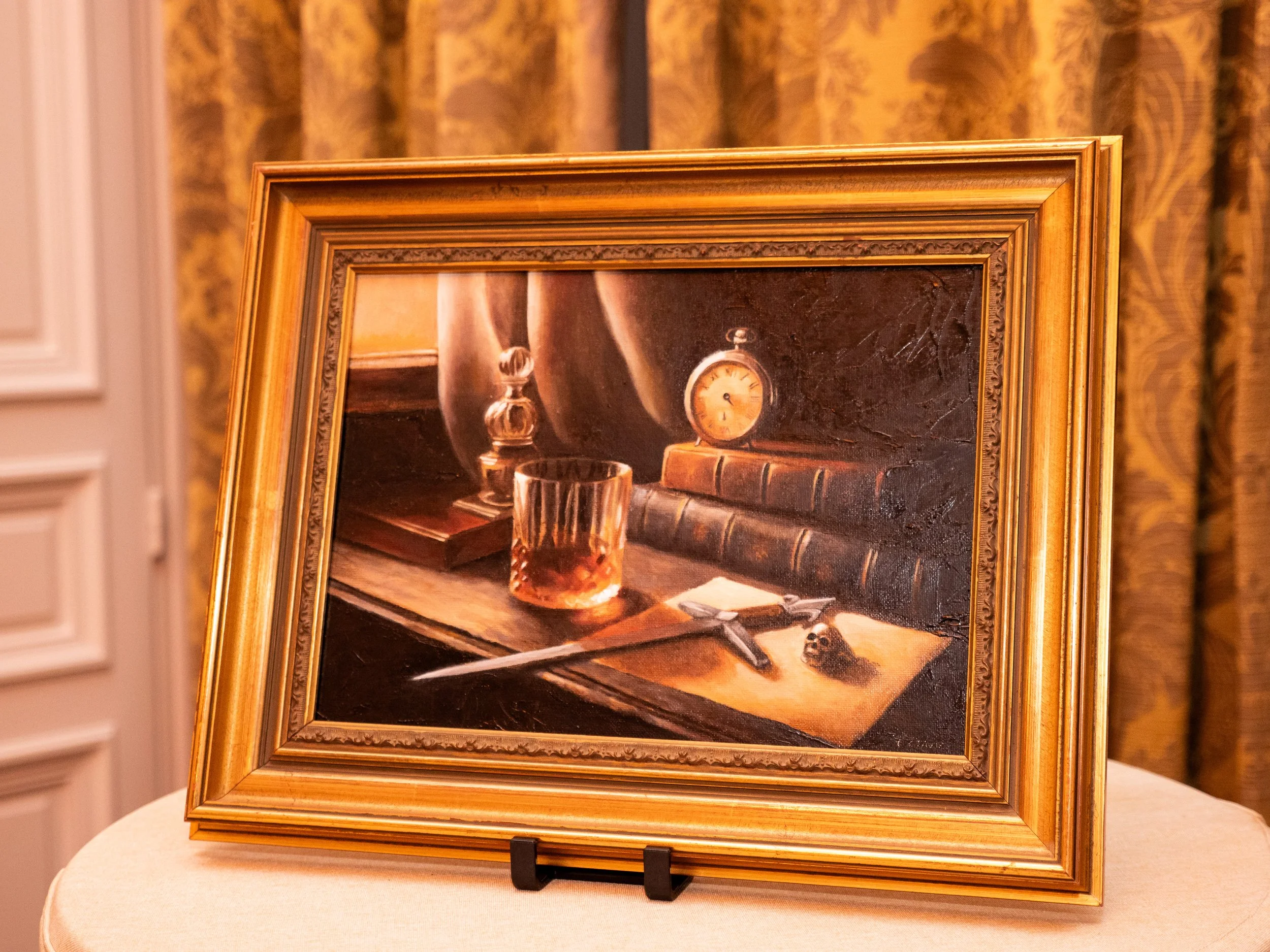 Une peinture représentant un bureau avec un livre, une montre, un verre, un couteau, un crâne miniature, une lampe de bureau et un tableau noir.
