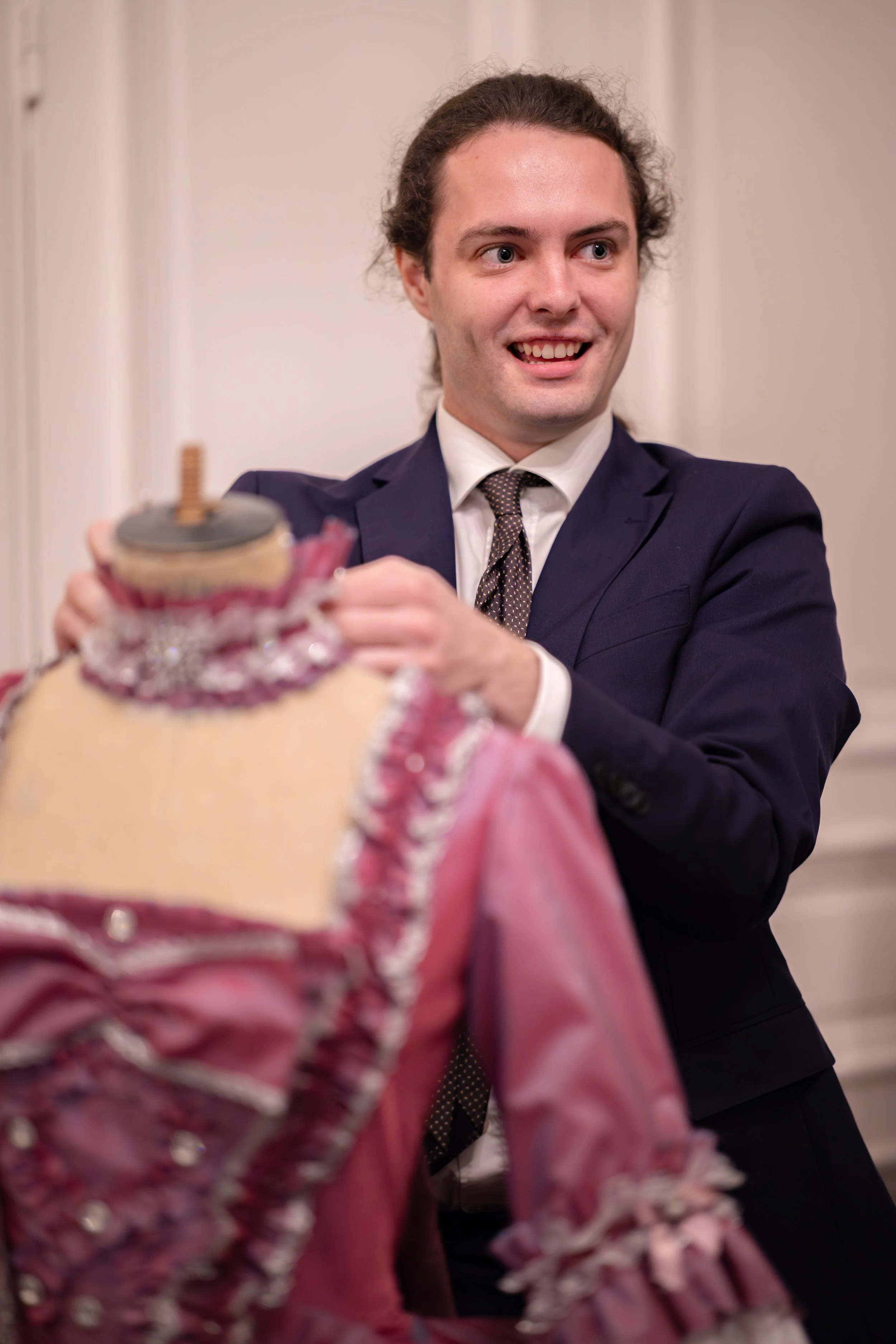 Jeune homme élégamment habillé en costume ajusté, manipulation sur une robe de poupée barbie.