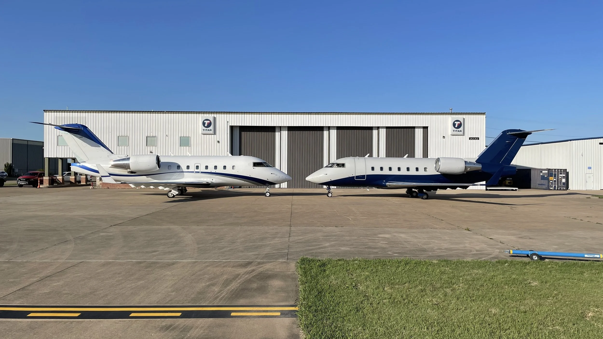 Two private jets parked on a tarmac in front of a Titan-branded hangar on a clear day.