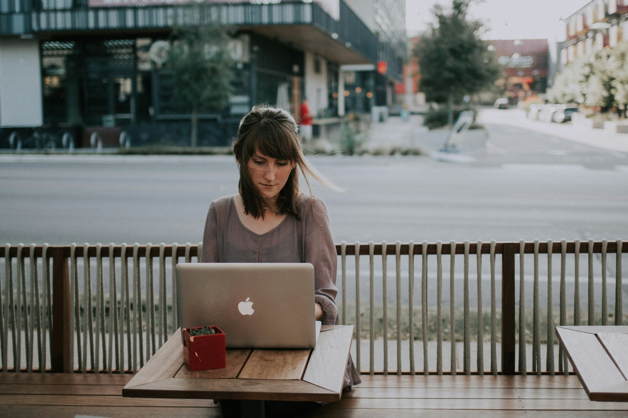 Person using laptop at outdoor cafe table with planter