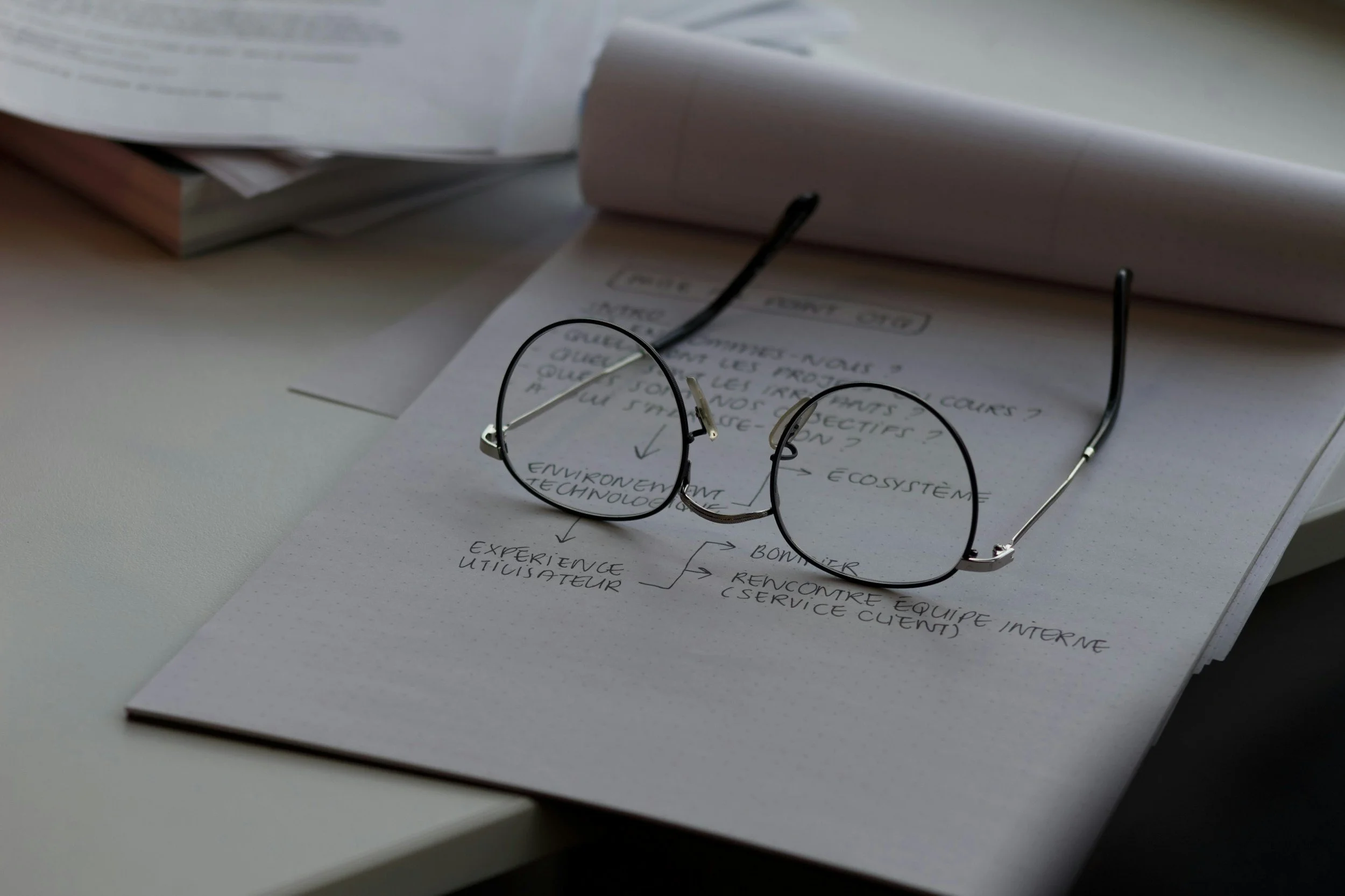 Round eyeglasses on a notebook with handwritten notes, placed on a desk.