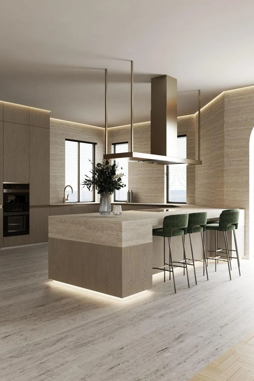 Modern kitchen with beige cabinetry, a central island with green bar stools, built-in oven, sink, and a range hood. Natural light enters from large windows, and decorative lighting highlights the minimalist design. A vase with flowers sits on the isl