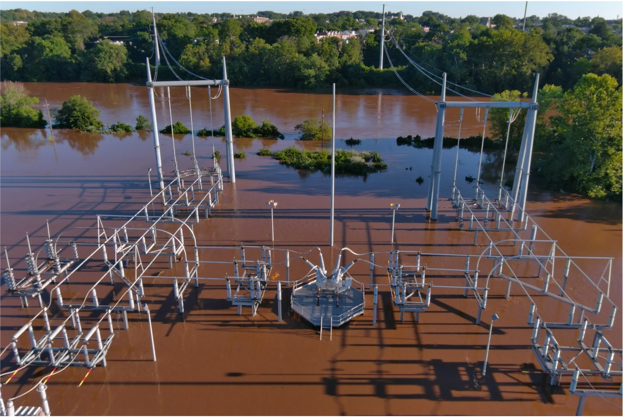 Aerial view of a flooded electric substation surrounded by rising floodwater, illustrating the physical infrastructure risk behind climate adaptation planning.
