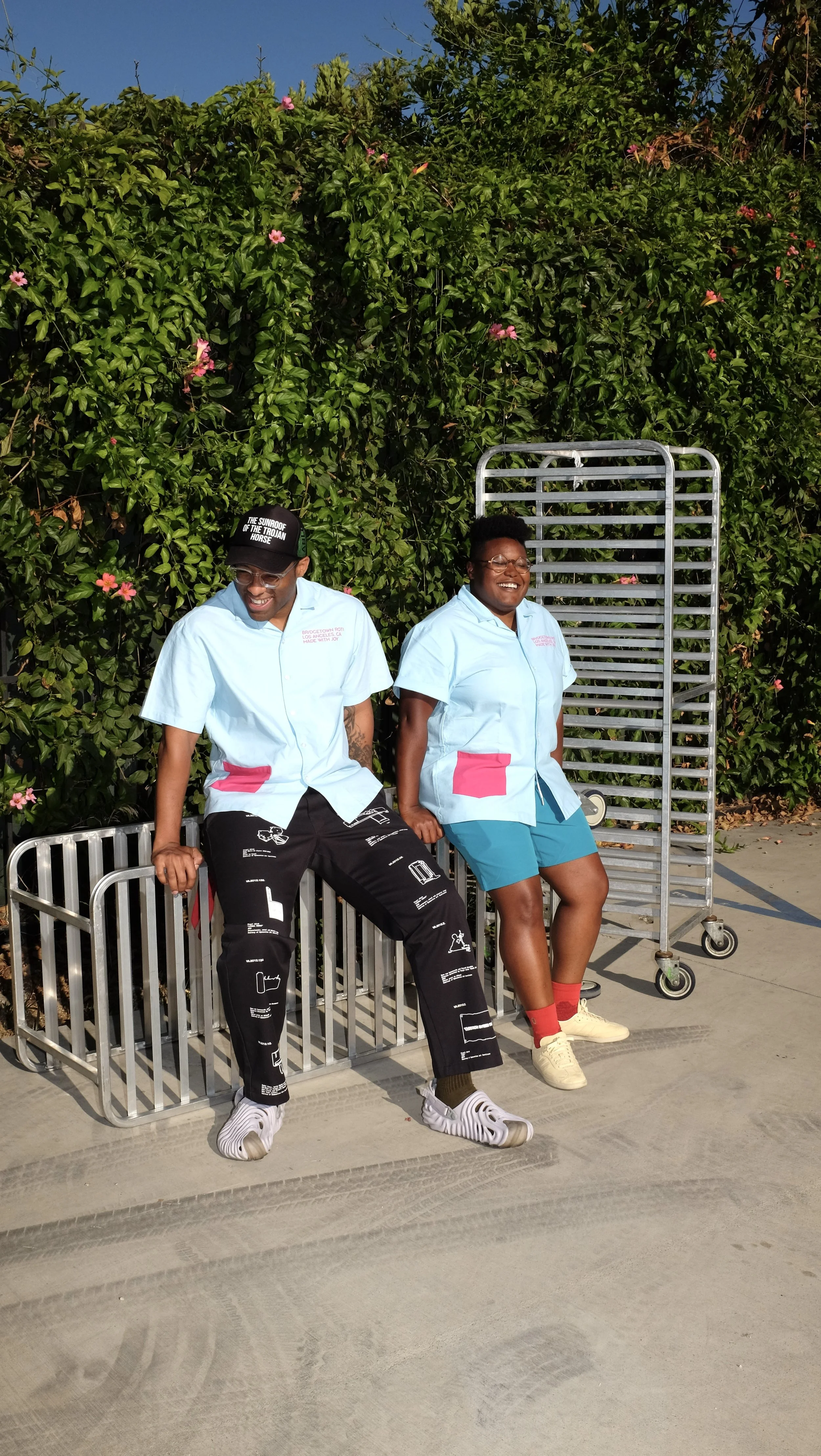 Pair wearing Rashida Holmes and Bridgetown Roti uniform shirt collaboration designed by Finery.