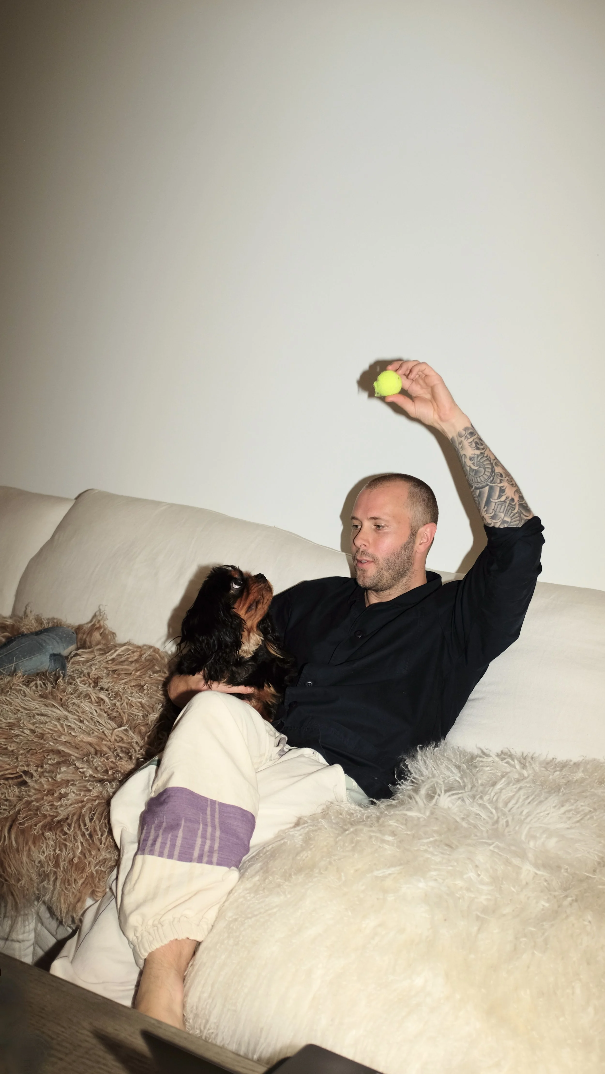 Mike Bagale sitting with dog on the couch wearing black chef coat designed by Finery.
