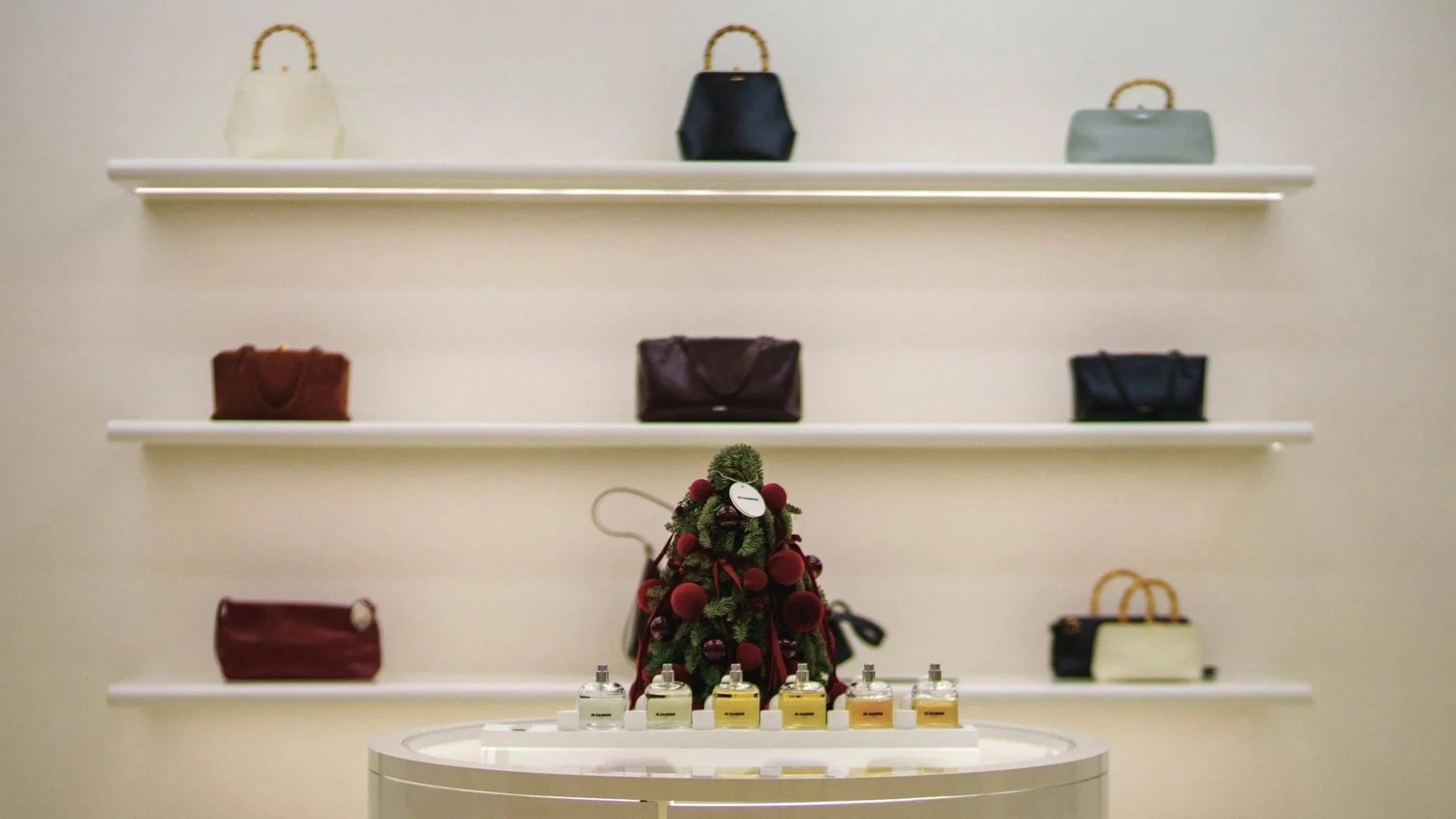 Vitrine avec plusieurs sacs à main colorés et des petits pots de parfum en bas.