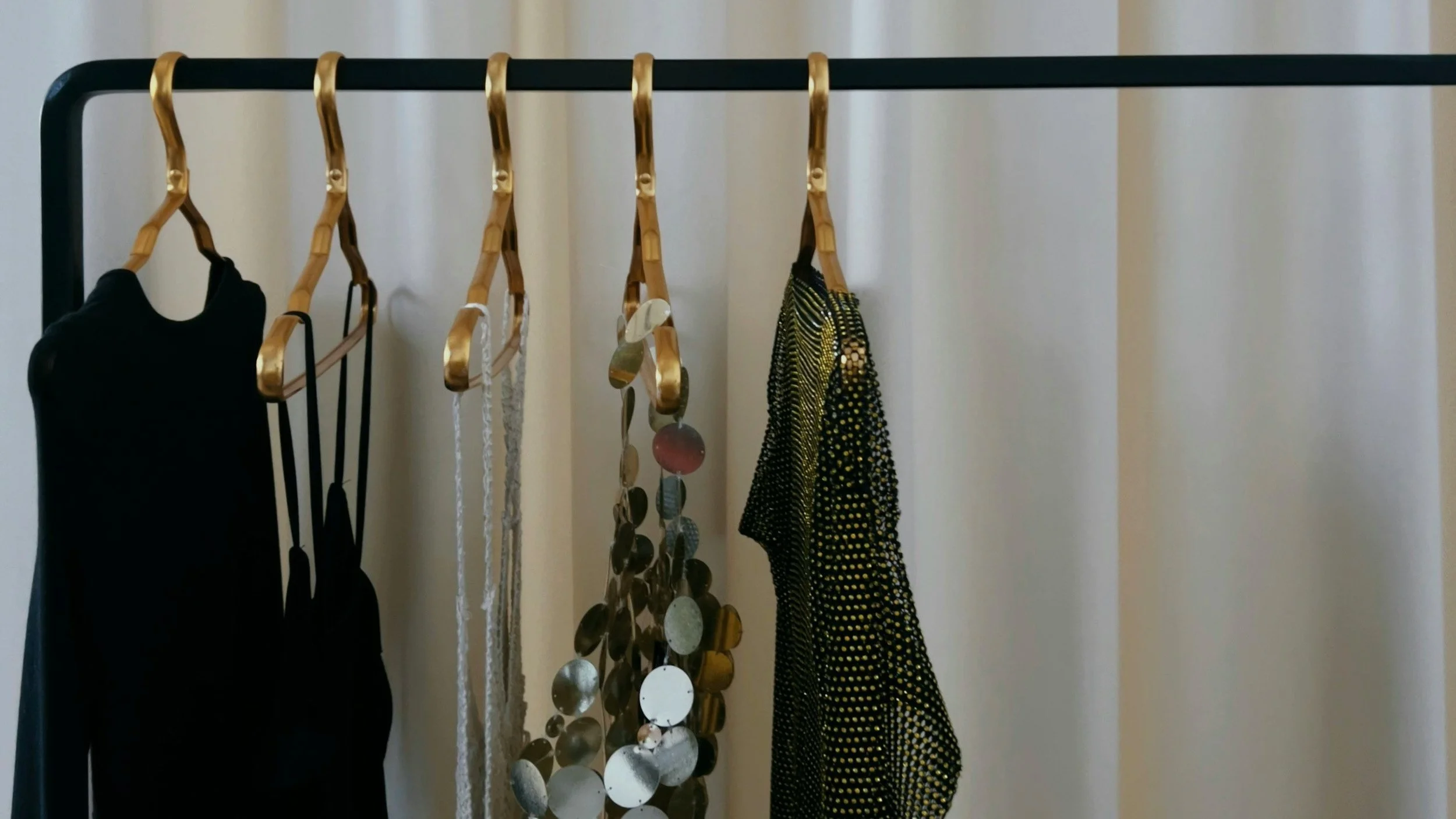 Cinq vêtements suspendus sur un portant noir, avec des cintres en bois.